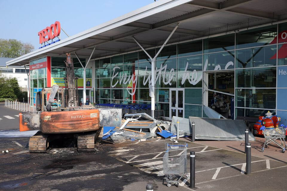 Burnt-out digger sits in front of the Tesco store in Crumlin, Co Antrim - 2019